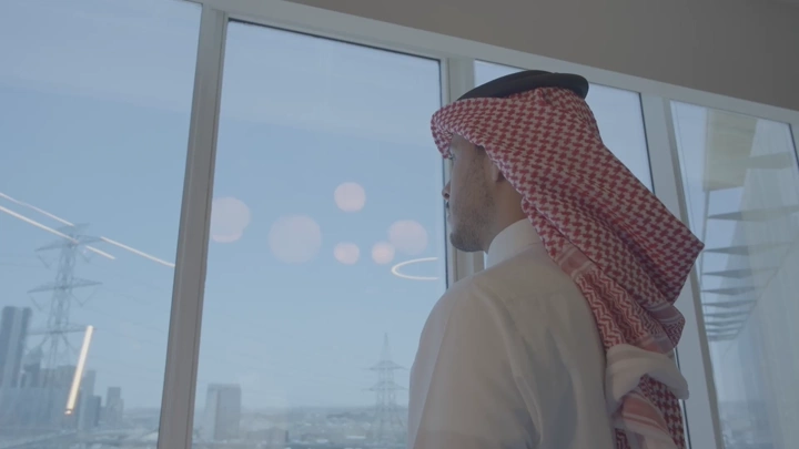 شاب ينظر إلى المدينة المالية من داخل مبنى في الرياض، لقطة داخلية.