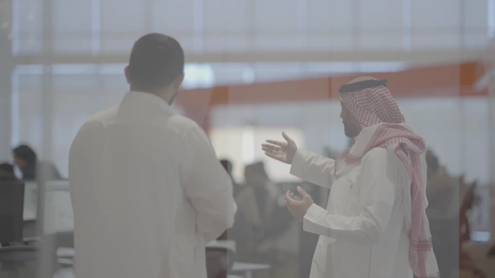 رجال يتحدثون في مكان عمل وامامهم خريطة المملكة العربية السعودية، لقطة من الخلف.