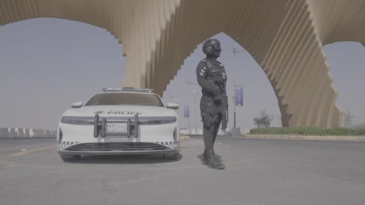 عسكري سعودي يقف بجانب سيارة شرطة عند بوابة الصقور في ملهم في الرياض، لقطة نهارية.