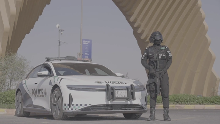 عسكري سعودي يقف بجانب سيارة شرطة عند بوابة الصقور في ملهم في الرياض، لقطة نهارية.