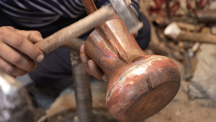 صانع يدق دلة نحاسية في ورشة، لقطة مقربة.