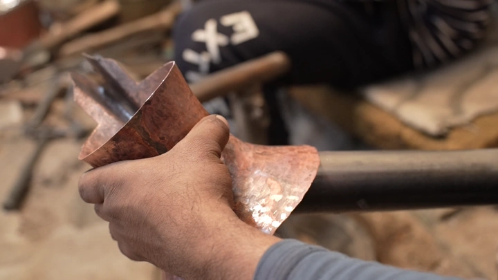 صانع يدوي يشكل دلة نحاسية في ورشة، لقطة قريبة.