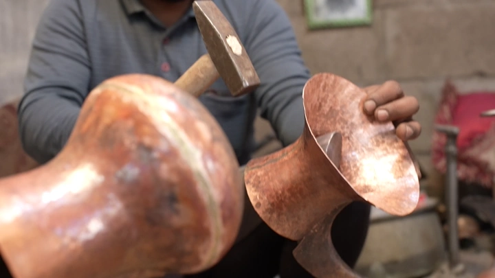 صانع يعمل على دلة نحاسية في ورشة، لقطة مقربة.