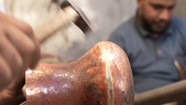 صانع يدق النحاس لتشكيل دلة في ورشة، لقطة مقربة.