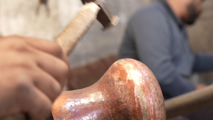 صانع يعمل على دلة نحاسية في ورشة، لقطة مقربة.