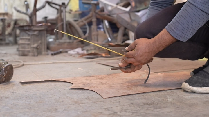 صانع يقيس النحاس لصنع دلة في ورشة، لقطة مقربة.