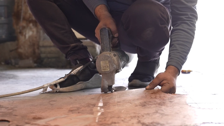 عامل يقطع مادة باستخدام أداة كهربائية في ورشة، لقطة قريبة.