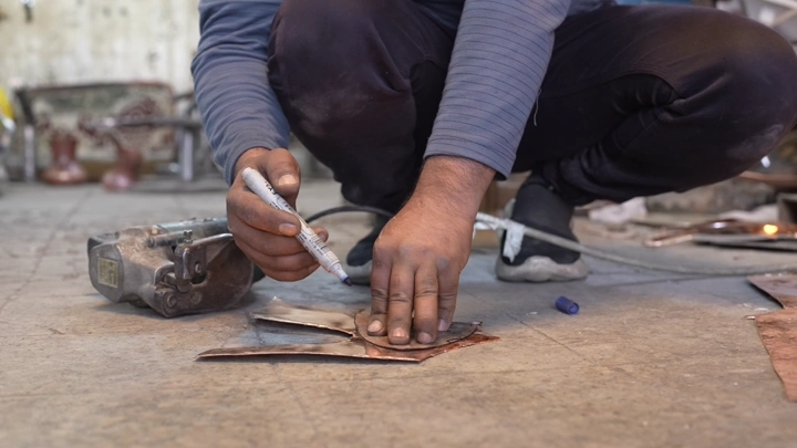 عامل يقطع المعدن لصناعة الدلة في ورشة، لقطة قريبة.