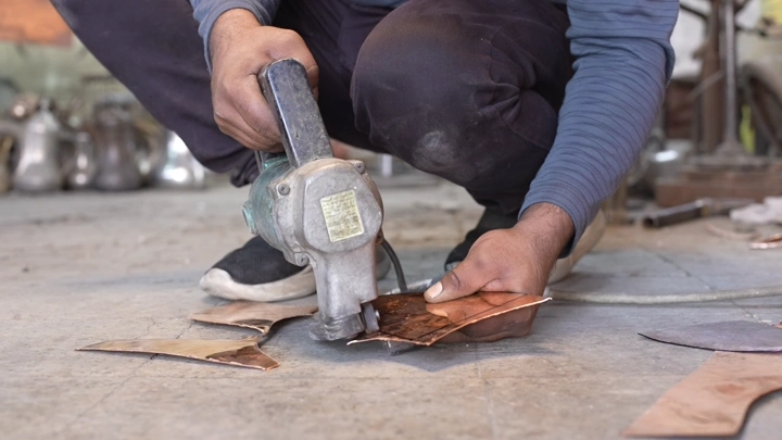 عامل يقطع صفائح معدنية لصناعة الدلة، لقطة قريبة.