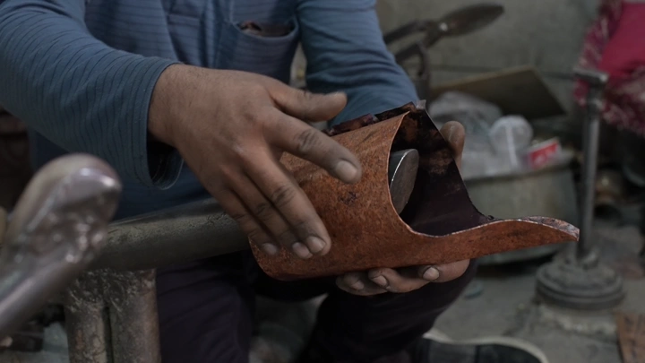 صانع يعمل على تشكيل دلة نحاسية في ورشة، لقطة مقربة.