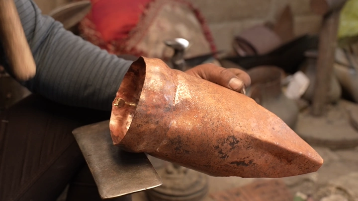 حرفي يعمل على تشكيل دلة نحاسية في ورشة تقليدية، لقطة مقربة.