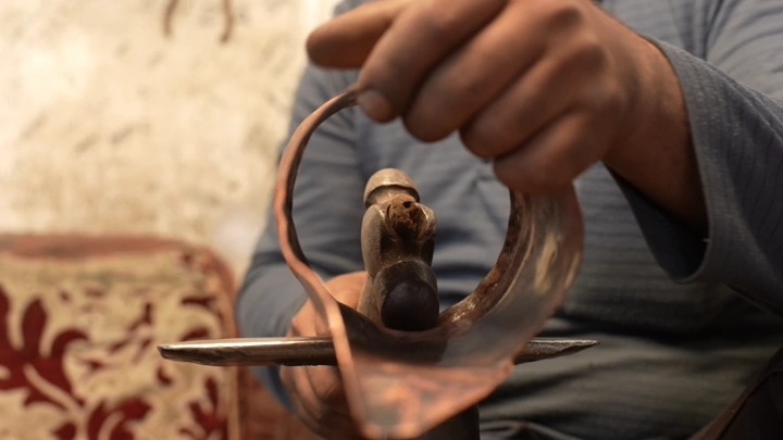 صانع يشكل دلة نحاسية يدويًا في ورشة تقليدية، لقطة مقربة.