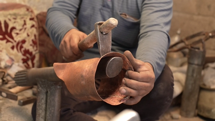 صانع يدق النحاس لصنع دلة في ورشة، لقطة مقربة.