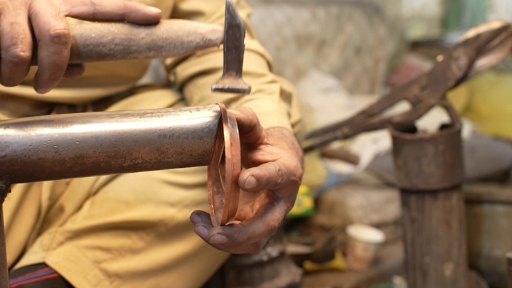 صانع يعمل على تشكيل دلة نحاسية يدوياً، لقطة مقربة.