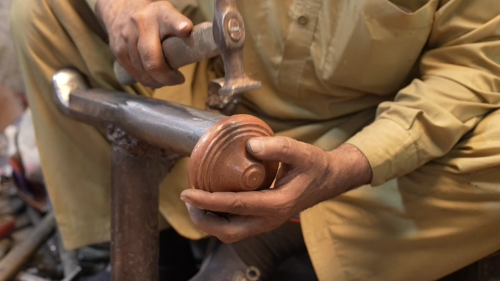 صانع يعمل على دلة نحاسية في ورشة، لقطة مقربة.