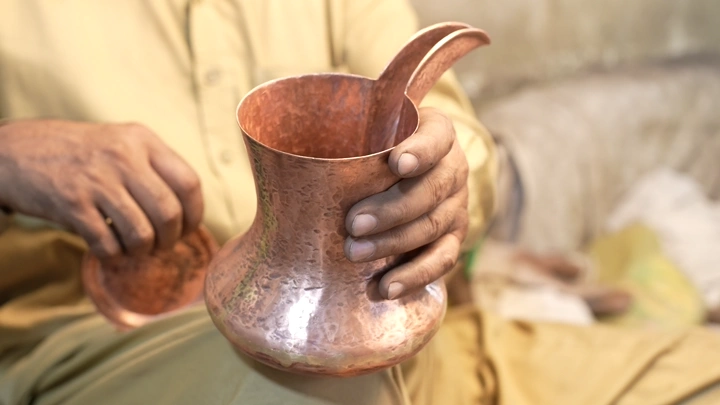حرفي يصنع دلة نحاسية يدوياً، تصوير قريب.