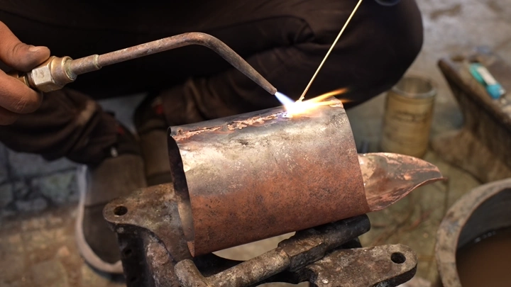عملية لحام جزء من دلة نحاسية في ورشة، لقطة مقربة.