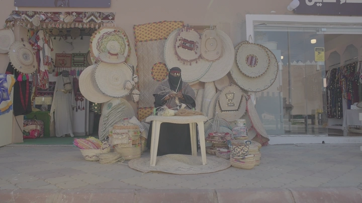 امرأة تصنع منتجات الخوص أمام متجر، لقطة نهارية.