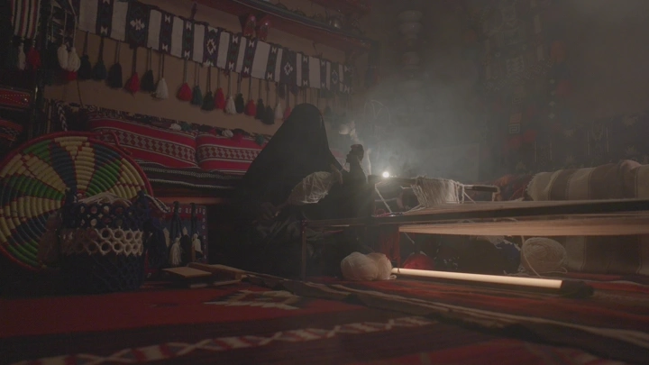 امرأة تنسج السدو في خيمة تقليدية، إضاءة خافتة.