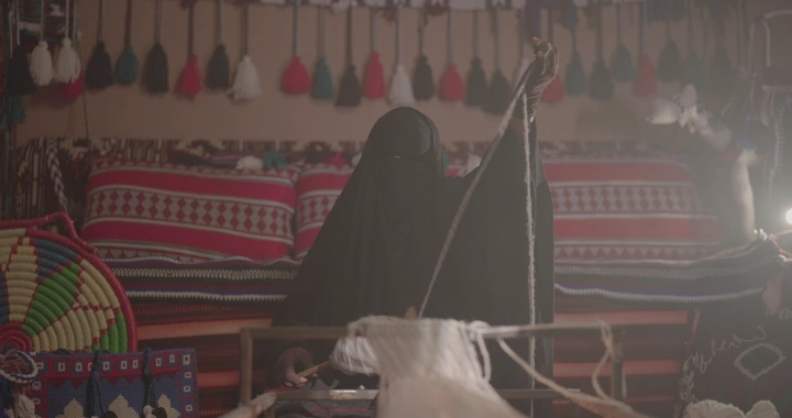 امرأة تعمل على نول سدو تقليدي في غرفة مزينة، لقطة داخلية.