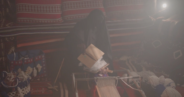 امرأة تقوم بنفش السدو في خيمة تقليدية، إضاءة خافتة.