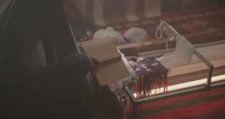 امرأة تعمل على نول سدو في غرفة مضاءة بشكل خافت، لقطة مقربة.