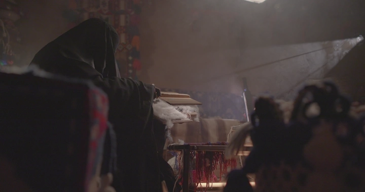 امرأة تعمل على حياكة السدو في غرفة تقليدية، إضاءة خافتة.