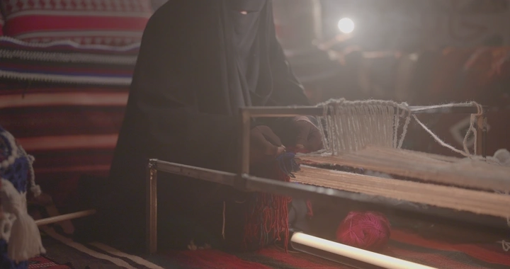 امرأة تنسج على نول سدو في غرفة مضاءة بشكل خافت.