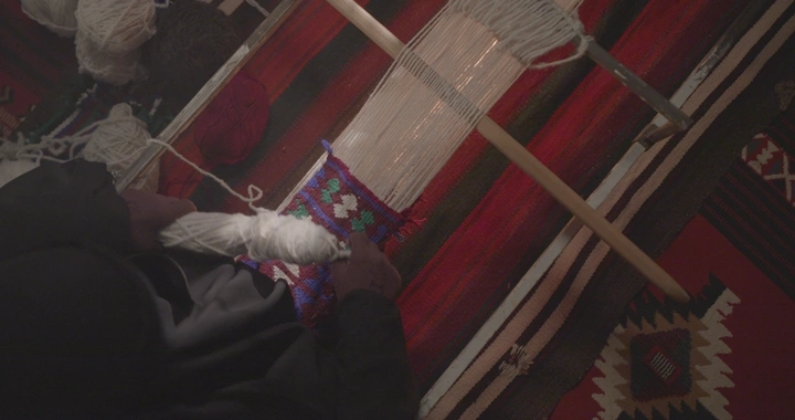 حياكة السدو التقليدية في غرفة مضاءة بشكل خافت، لقطة علوية.