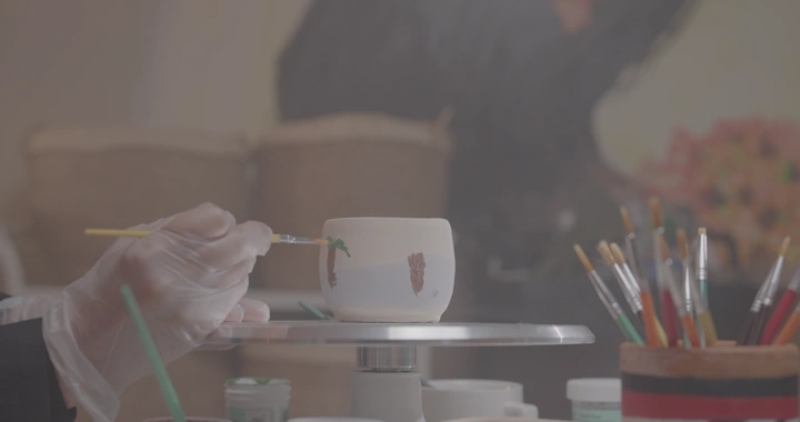 يد تلوّن فنجان فخار في ورشة، لقطة مقربة.