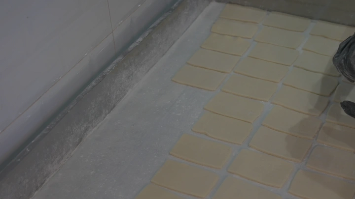 قطع عجين مربعة مرتبة على سطح عمل، لقطة مقربة.