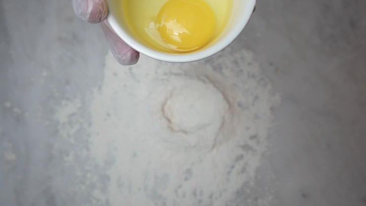 بيضة في وعاء فوق دقيق على سطح مطبخ، لقطة علوية.