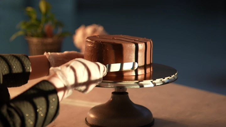 تزيين كيكة شوكولاتة على طاولة في إضاءة ناعمة، لقطة قريبة.