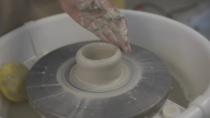 يد تشكل الطين على عجلة الفخار، لقطة مقربة.