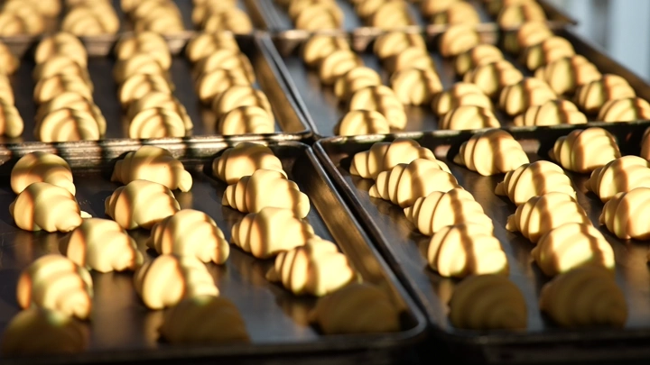 صواني خبز مليئة بالكرواسان الذهبي في المخبز، لقطة مقرّبة.