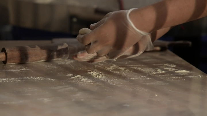 يد تعجن العجين على طاولة خشبية، لقطة قريبة.