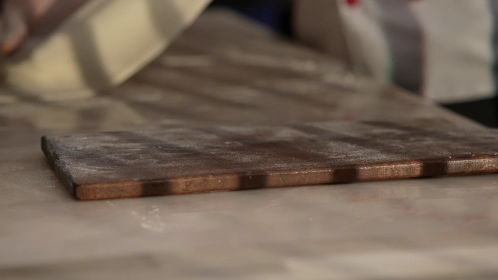 عجينة تُفرد على لوح خشبي في مطبخ، لقطة قريبة.