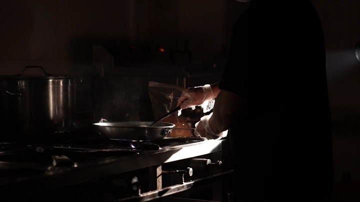 طاهٍ يطبخ في مطبخ مظلم، لقطة جانبية.