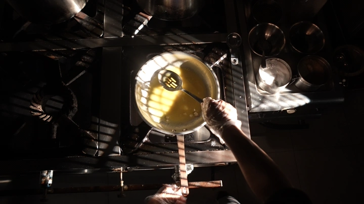 شخص يطبخ زبدة في مقلاة على موقد، إضاءة خافتة.