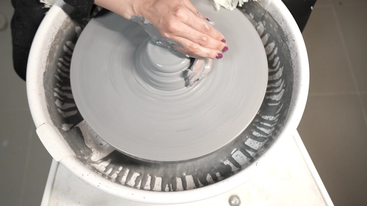يد تشكل الطين على عجلة فخار، لقطة من الأعلى.