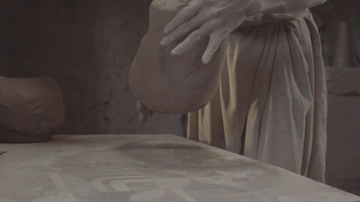 يد تشكل الطين على طاولة في ورشة، لقطة مقربة.