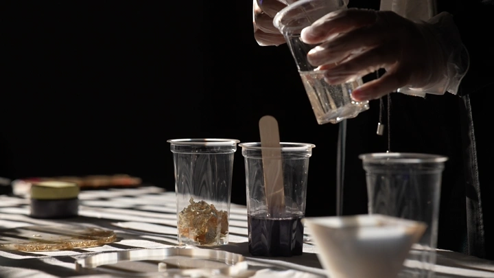 شخص يخلط مواد الريزن في أكواب بلاستيكية على طاولة، لقطة قريبة.