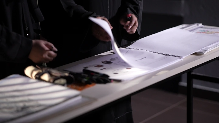 شخص يقلب مخططات على طاولة، إضاءة خافتة، لقطة قريبة.