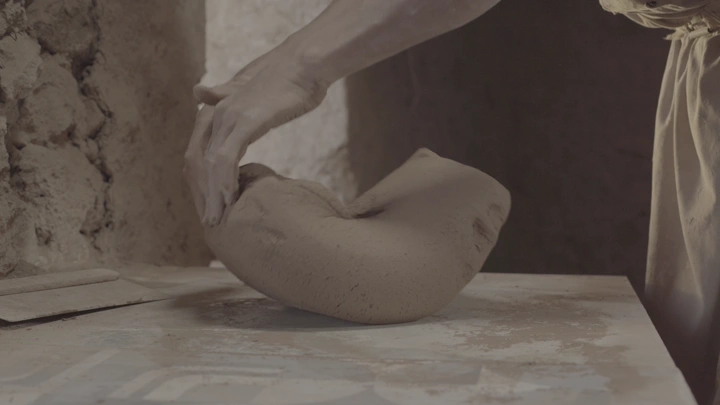 يد تشكل الطين على طاولة خشبية، لقطة قريبة.