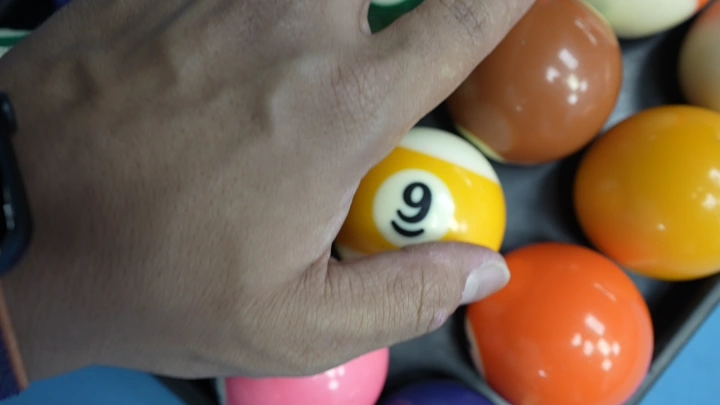 يد تمسك كرة بلياردو على طاولة زرقاء، لقطة مقربة.