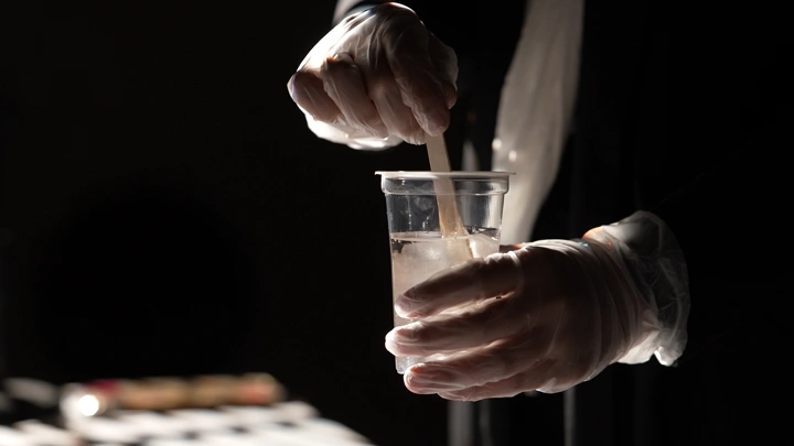 شخص يخلط الريزن في كوب بلاستيكي، إضاءة خافتة.