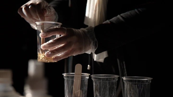 شخص يخلط مادة الريزن في كوب بلاستيكي، إضاءة خافتة.