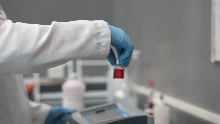 يد في قفاز تحمل أنبوب اختبار في مختبر، لقطة مقربة.