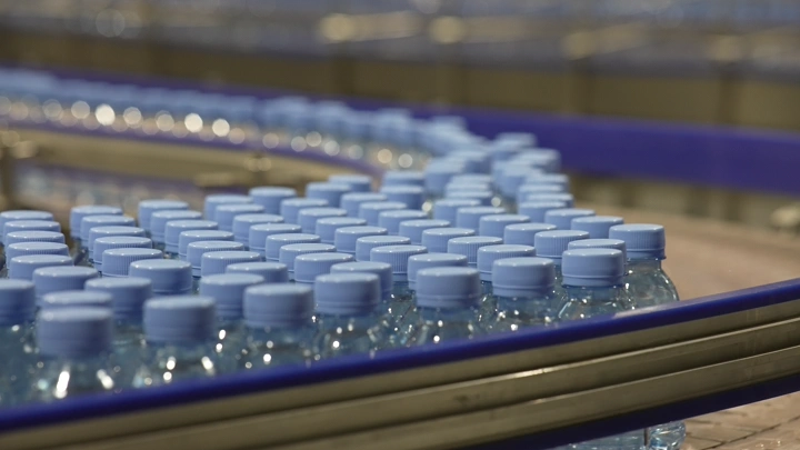 زجاجات مياه على خط إنتاج في مصنع، لقطة مقربة.