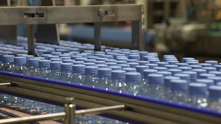 زجاجات مياه على خط إنتاج في مصنع، لقطة مقربة.